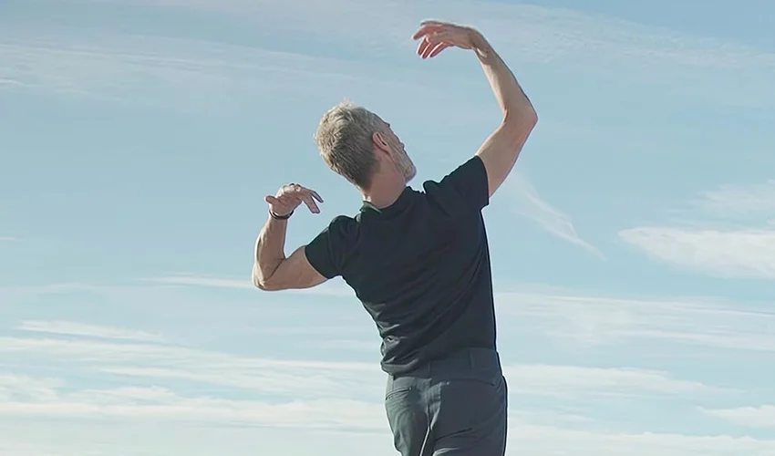 still from a film of a person from behind wearing a short sleeve dark t shirt striking a pose looking away from the camera